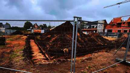 Foto van de bouwplaats met op de voorgrond bouwhekken en daarachter een bouwplaats van zand met eerste graafwerkzaamheden.