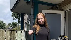 Een zonnige foto van Laura bij de achterdeur van haar woning, naast haar een werkbank voor het klussen.