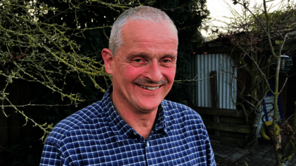 Tom van Woerden vanaf borsthoogte staande in een achtertuin. Lachend. Foto vanaf borsthoogte