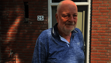 Piet voor zijn woning (vanaf borsthoogte). blauwe polo. Zon schijnt door de bladeren van de bomen en je ziet de schaduwen van de blaadjes op de muur en op Piet.