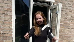 Een zonnige foto van Laura bij het achterraam van haar woning. Laura heeft de huissleutel en een verfroller in haar hand.