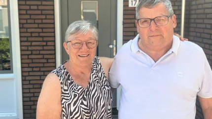Jan en Francie in de zon voor hun gerenoveerde woning. Vanaf hun middel tot hoofd op de foto. Jan met witte polo. Francie met een zwart/witte mouwlos hes. Beiden dragen een bril.