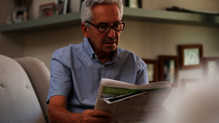 Oudere man zit op de bank en leest de krant