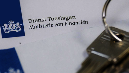 Stukje van een envelop van overheid met blauwe logo en tekst Dienst Toeslagen. Op de envelop ligt een ring met 2 huissleutels.