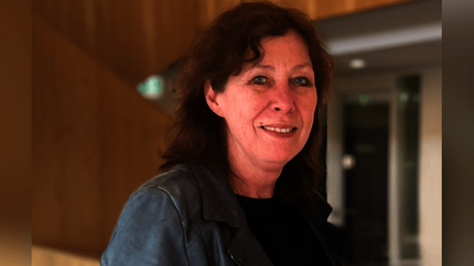 Foto van Joke Abbring met een lichte glimlach. Donkere kleding. Vanaf borsthoogte omhoog. Beetje zijwaarts staand.