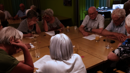 Groep oudere huurders om een grote tafel bezig met een quiz. Op de achtergrond nog een groep.