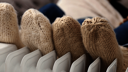 Twe paar voeten in dikke beige sokken tegen een verwarming.