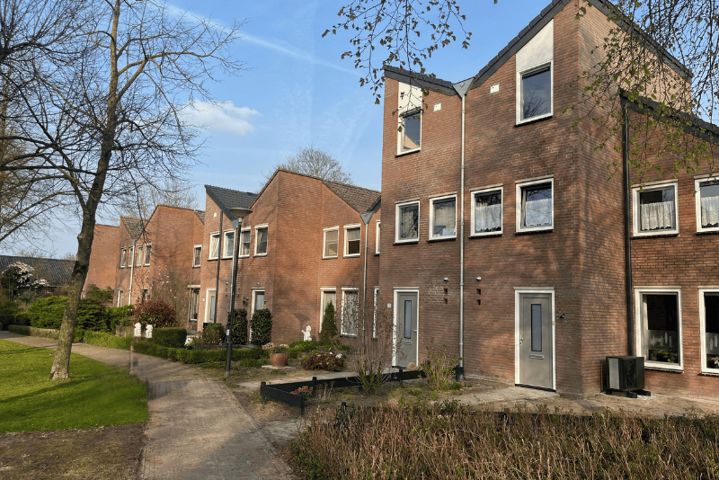 Foto van een rijtje gerenoveerde woningen aan een groen hofje in de zon