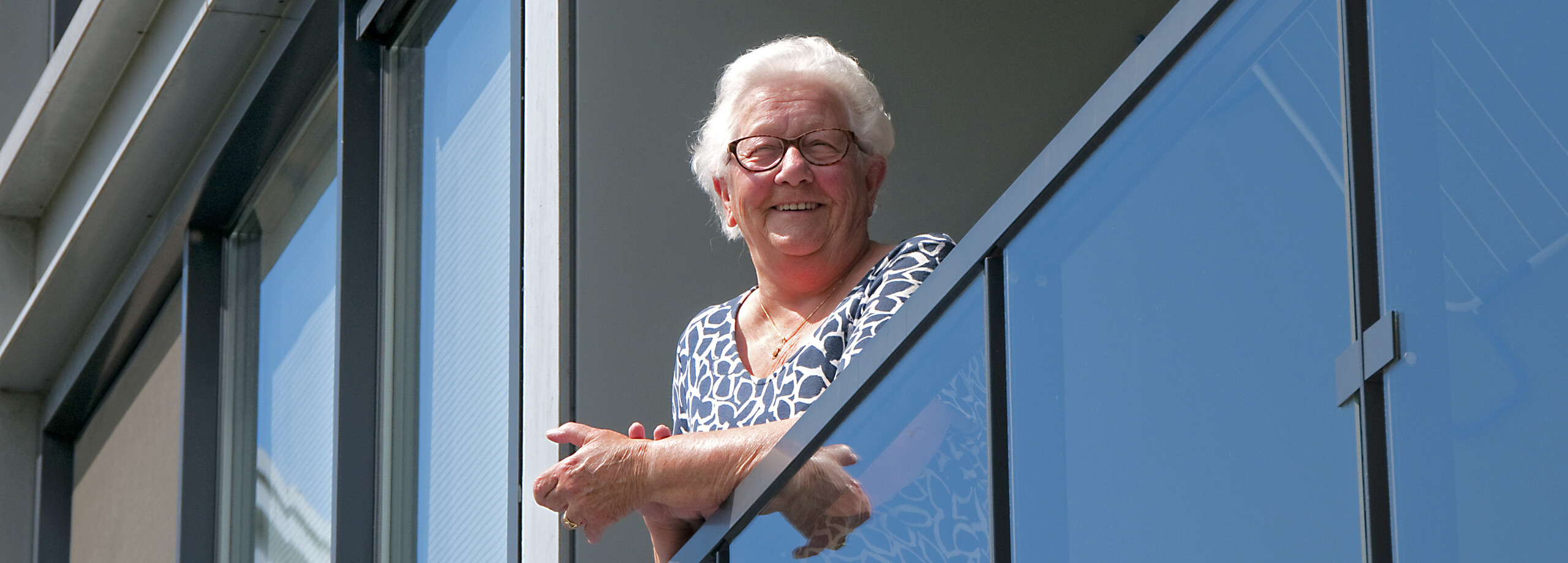 Foto van huurder Mien die lachend op de rand van haar balkon hangt.
