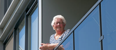 Foto van huurder Mien die lachend op de rand van haar balkon hangt.