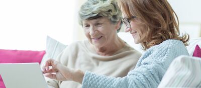 Seniore moeder en dochter van in de 40 zitten samen op de bank. Lachen en kijken naar laptop en papieren