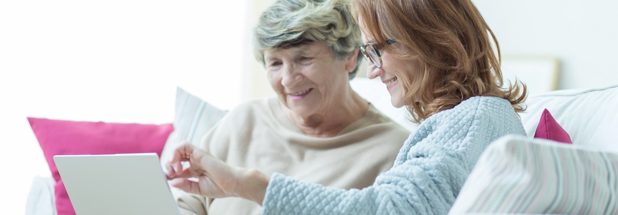 Seniore moeder en dochter van in de 40 zitten samen op de bank. Lachen en kijken naar laptop en papieren